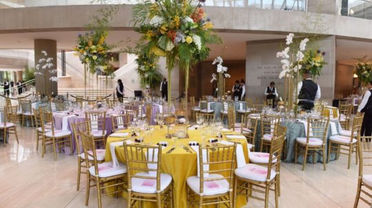 Últimos preparativos en el vestíbulo este del Meyerson para un evento inspirado en la primavera. Las mesas son amarillas, verde espuma de mar y lila.