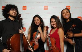 Teens holding their instruments and posing for a photo at a DSO step and repeat