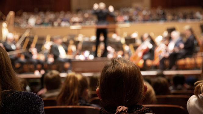 Students watching the stage, photographed from behind.