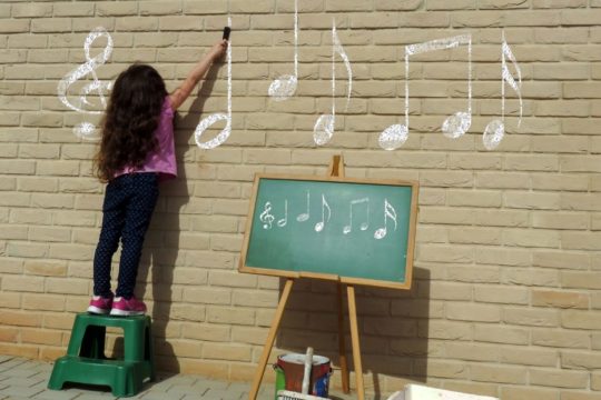 young girl draws musicial notes on a wall