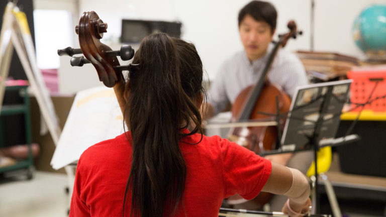 La chica toca el violonchelo delante del instructor