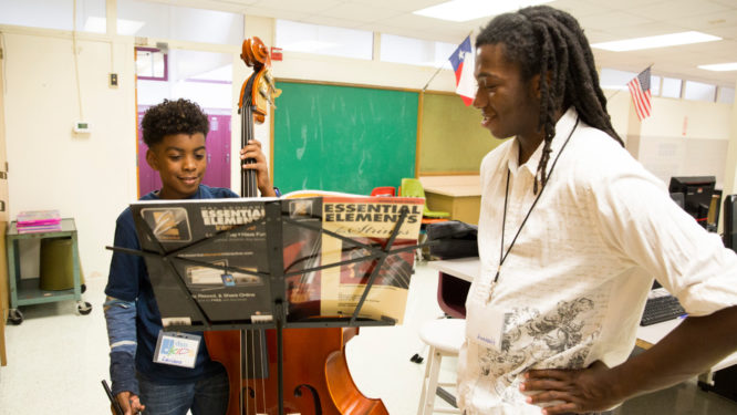 Boy holds bass standing next to instructor