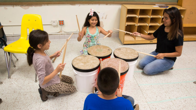 Tres niños y un instructor tocan los tambores
