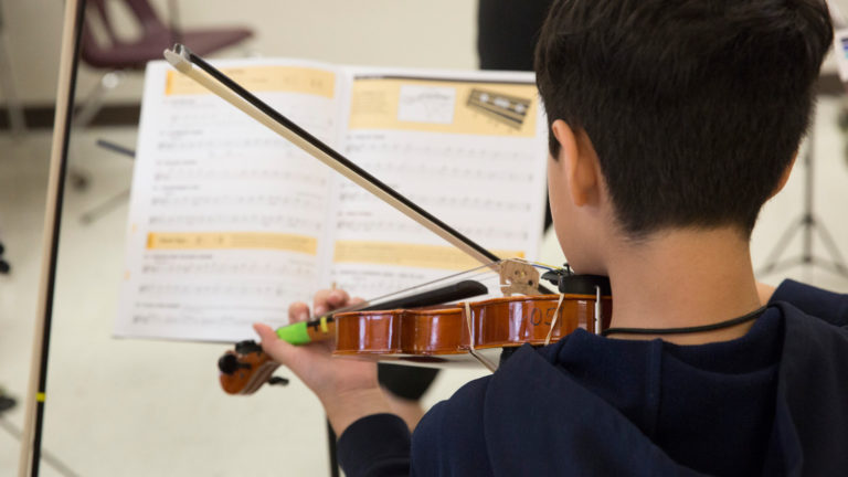El chico toca el violín mientras mira las partituras