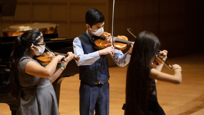Three children perform violin on stage