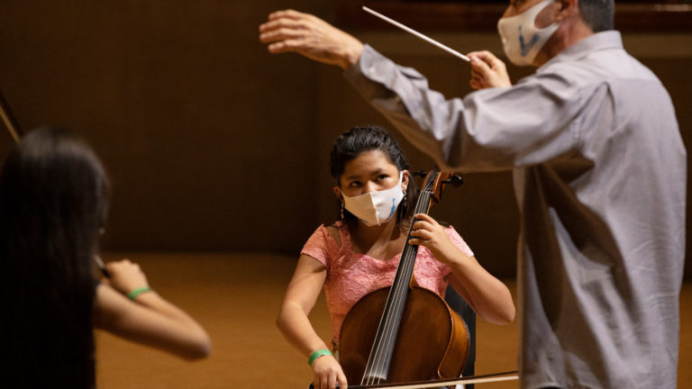 Girl plays cello on stage next to conductor