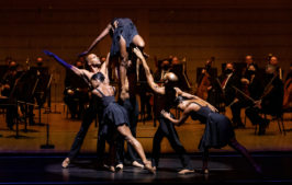 Six dancers performing in front of orchestra