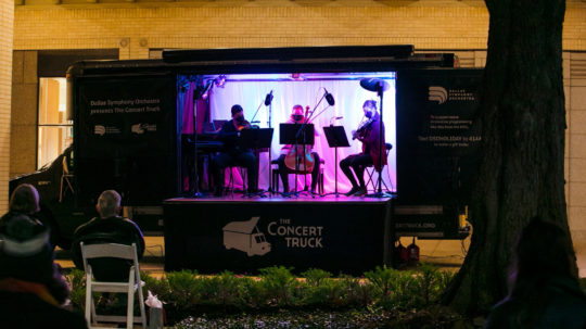 Three musicians perform sitting in concert truck