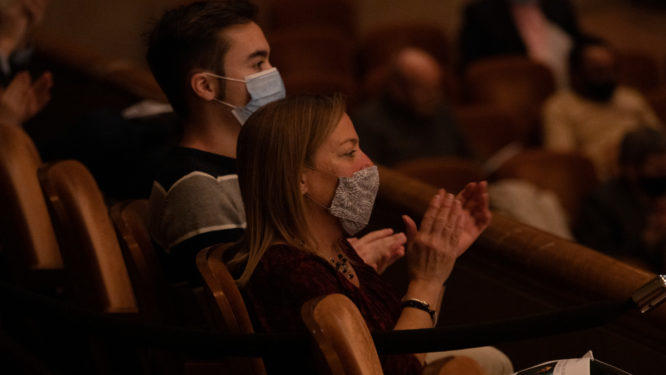 Un hombre y una mujer con máscaras faciales se sientan en el público